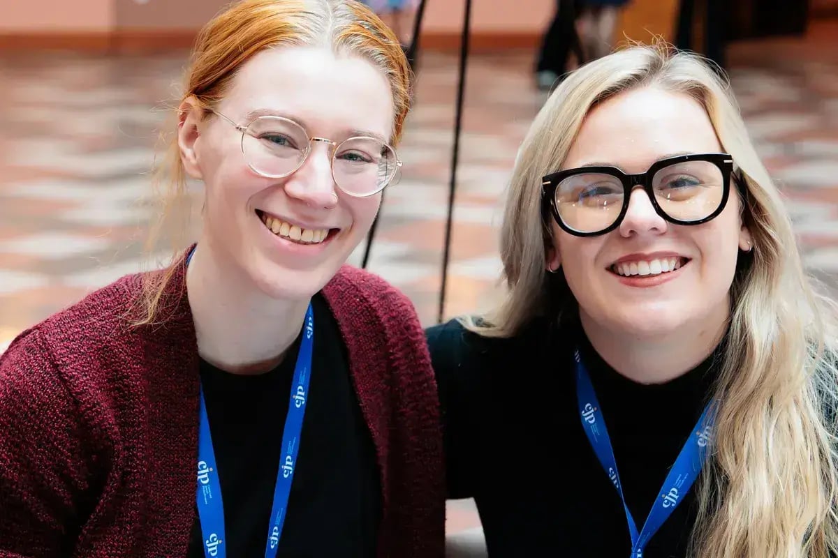 Two young professionals smiling and talking at a workplace conference.