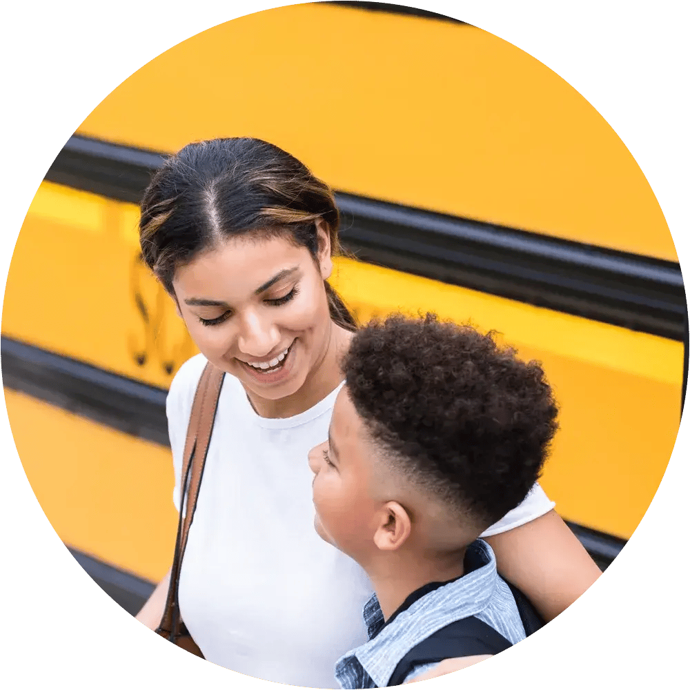 Parent and child standing near a school bus.