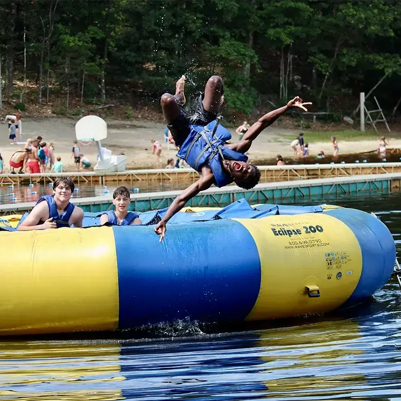 A preteen kid is jumping off a floating raft in a lake with his friends at Jewish summer camp.