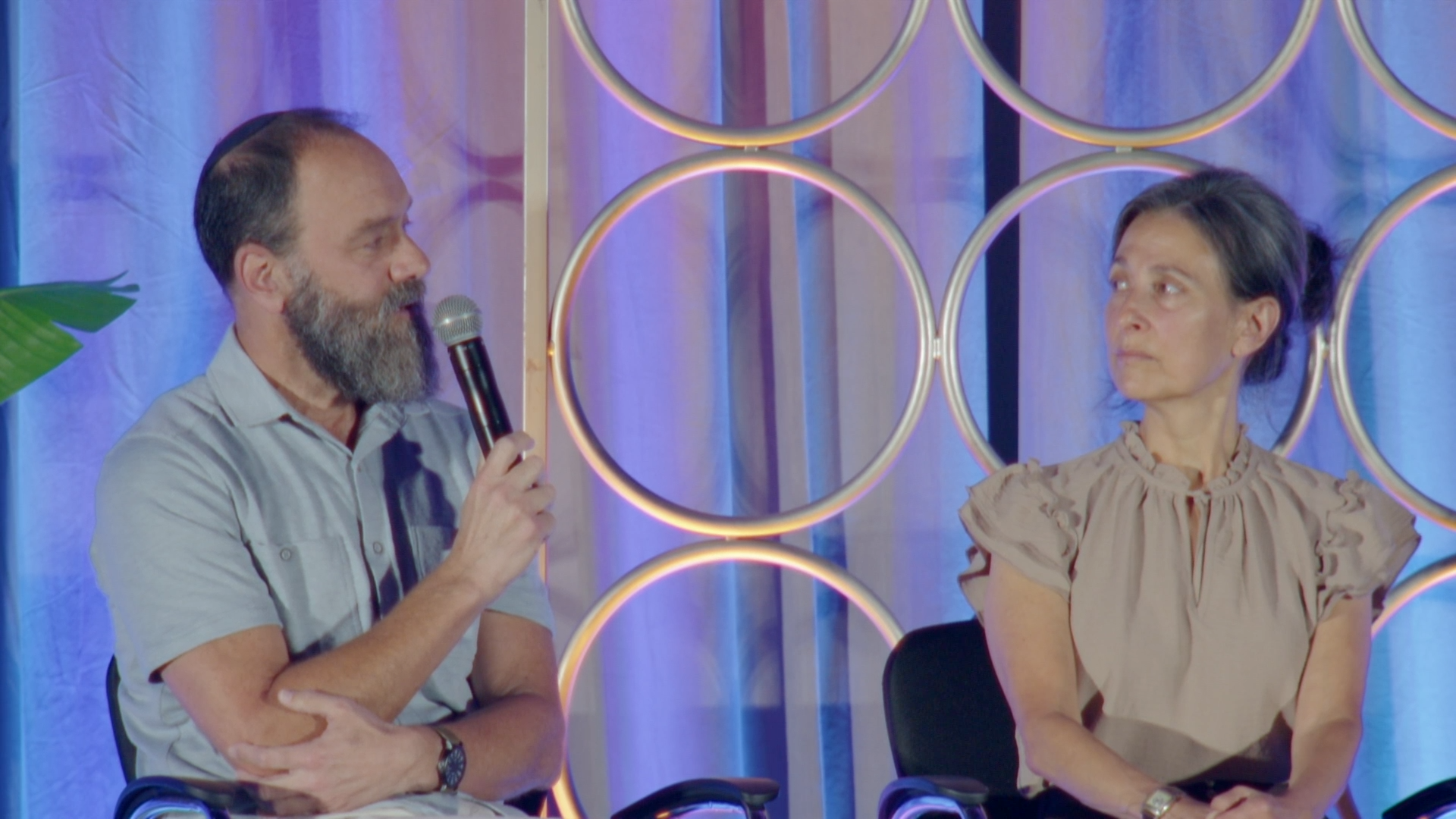 Rachel Goldberg-Polin and Jon Polin speaking on stage in front of a set of circular lights.