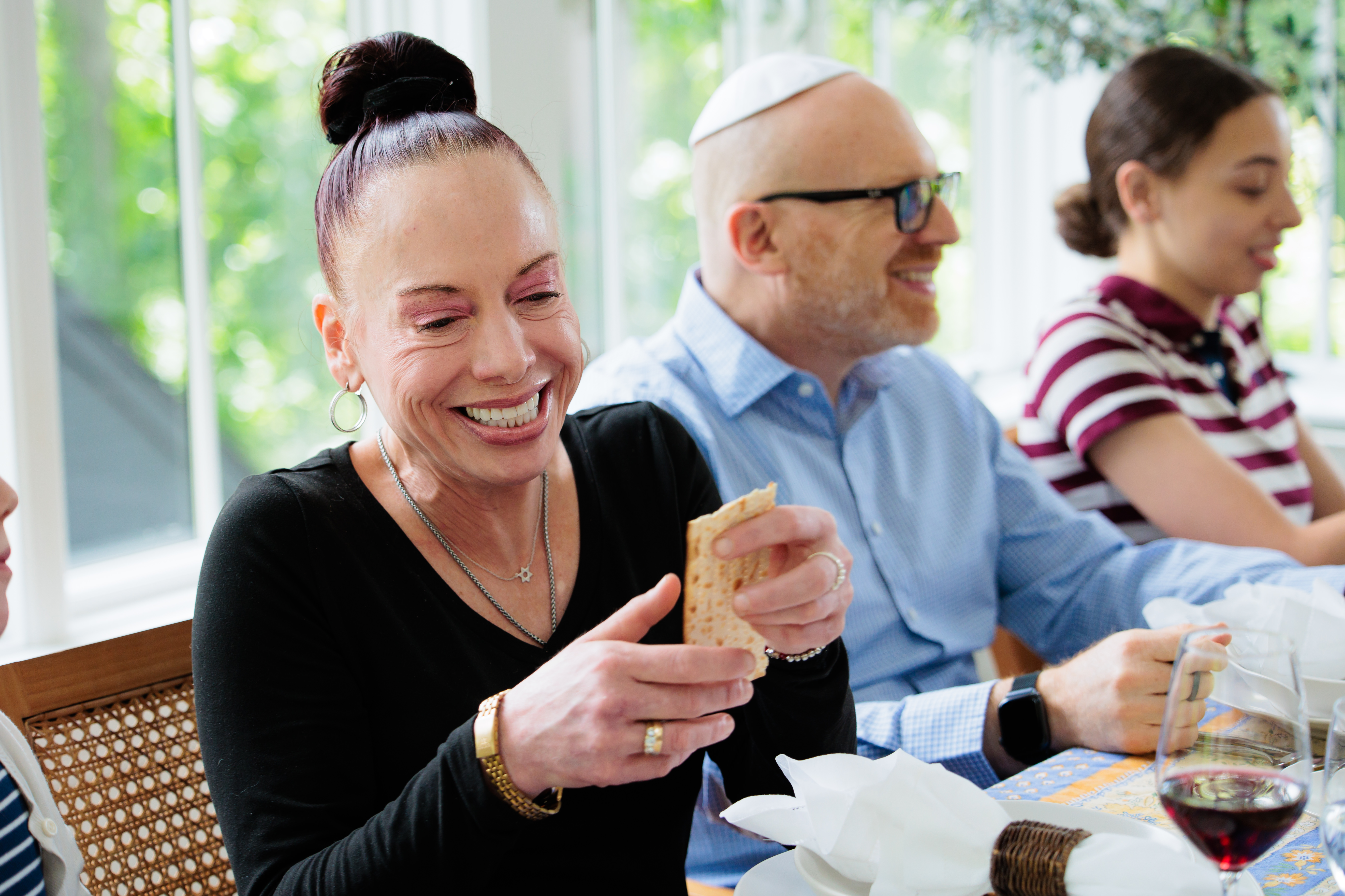 Image: A family smiles and breaks matzah at the dinner table.